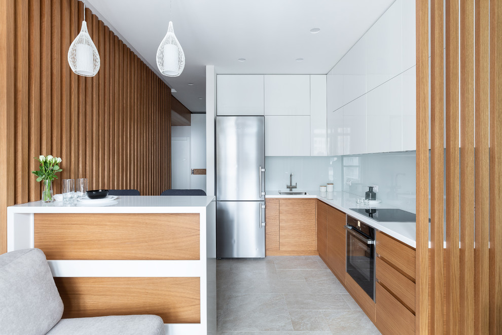 Photo of a mid-sized contemporary l-shaped separate kitchen in Saint Petersburg with an undermount sink, flat-panel cabinets, medium wood cabinets, solid surface benchtops, white splashback, glass tile splashback, porcelain floors, beige floor, white benchtop, black appliances and a peninsula.