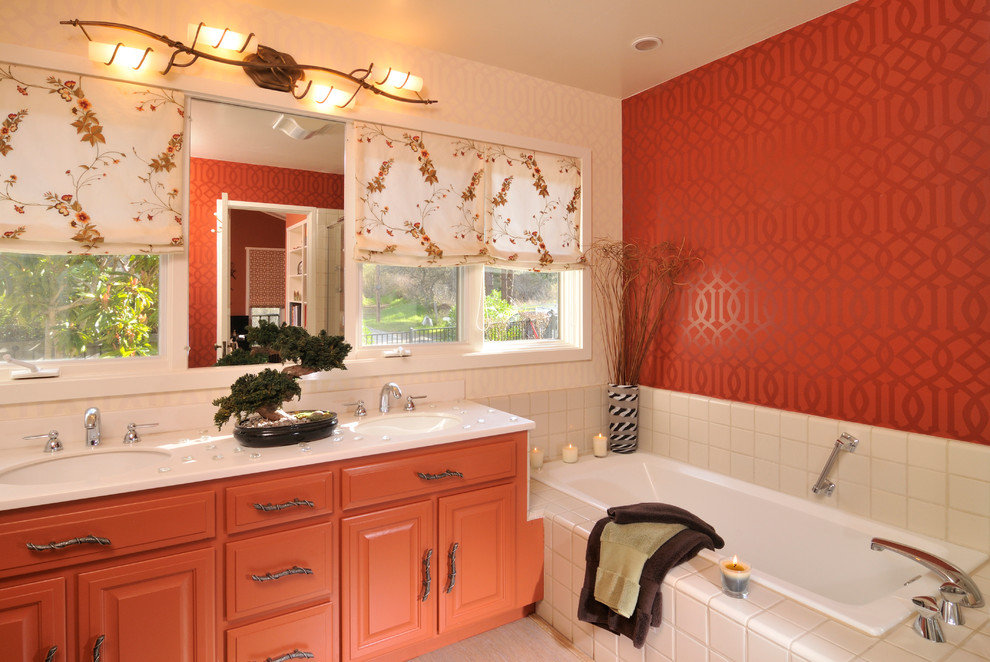 Design ideas for a mid-sized transitional master bathroom in Other with a drop-in tub, orange cabinets, raised-panel cabinets, white tile, ceramic tile, orange walls, porcelain floors, an undermount sink, solid surface benchtops, white benchtops, a built-in vanity and wallpaper.