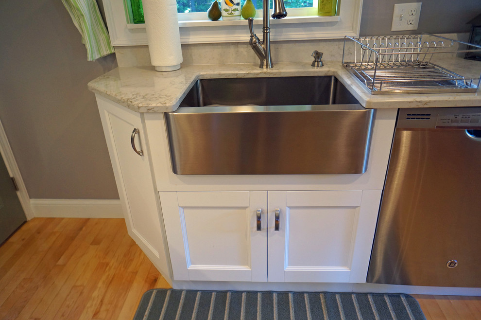 Inspiration for a large transitional l-shaped light wood floor eat-in kitchen remodel in Boston with a farmhouse sink, shaker cabinets, white cabinets, quartz countertops, white backsplash, stone slab backsplash, stainless steel appliances and an island