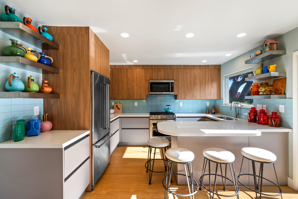 Photo of a midcentury u-shaped kitchen in Other with a double-bowl sink, flat-panel cabinets, medium wood cabinets, blue splashback, stainless steel appliances, medium hardwood floors, a peninsula and white benchtop.