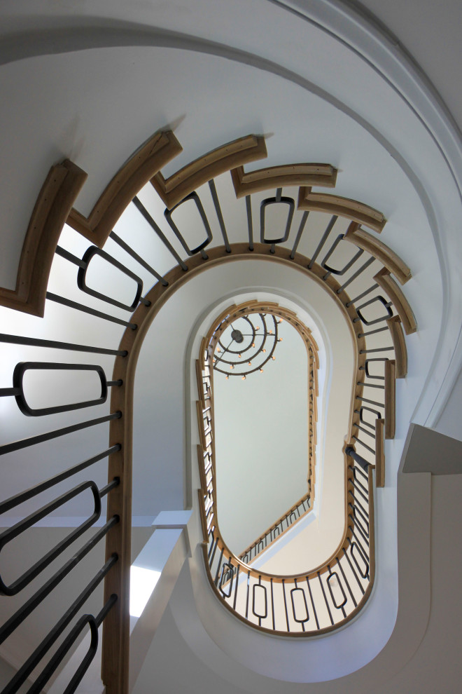 Свежая идея для дизайна: огромная изогнутая деревянная лестница в стиле неоклассика (современная классика) с деревянными ступенями, перилами из смешанных материалов и панелями на стенах - отличное фото интерьера
