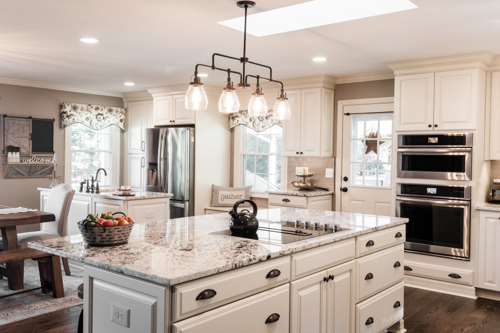 This is an example of an expansive country eat-in kitchen in Baltimore with a farmhouse sink, white cabinets, granite benchtops, medium hardwood floors, multiple islands and brown floor.