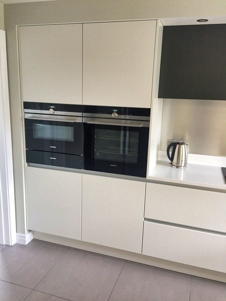 Inspiration for a mid-sized contemporary u-shaped eat-in kitchen in Cambridgeshire with an undermount sink, flat-panel cabinets, grey cabinets, quartzite benchtops, black appliances, ceramic floors, a peninsula, grey floor and white benchtop.