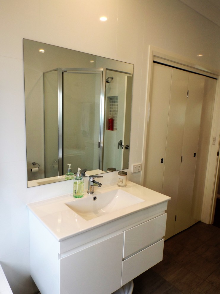 Photo of a mid-sized modern kids bathroom in Central Coast with flat-panel cabinets, white cabinets, a drop-in tub, a corner shower, a two-piece toilet, white tile, cement tile, white walls, cement tiles, a wall-mount sink and granite benchtops.