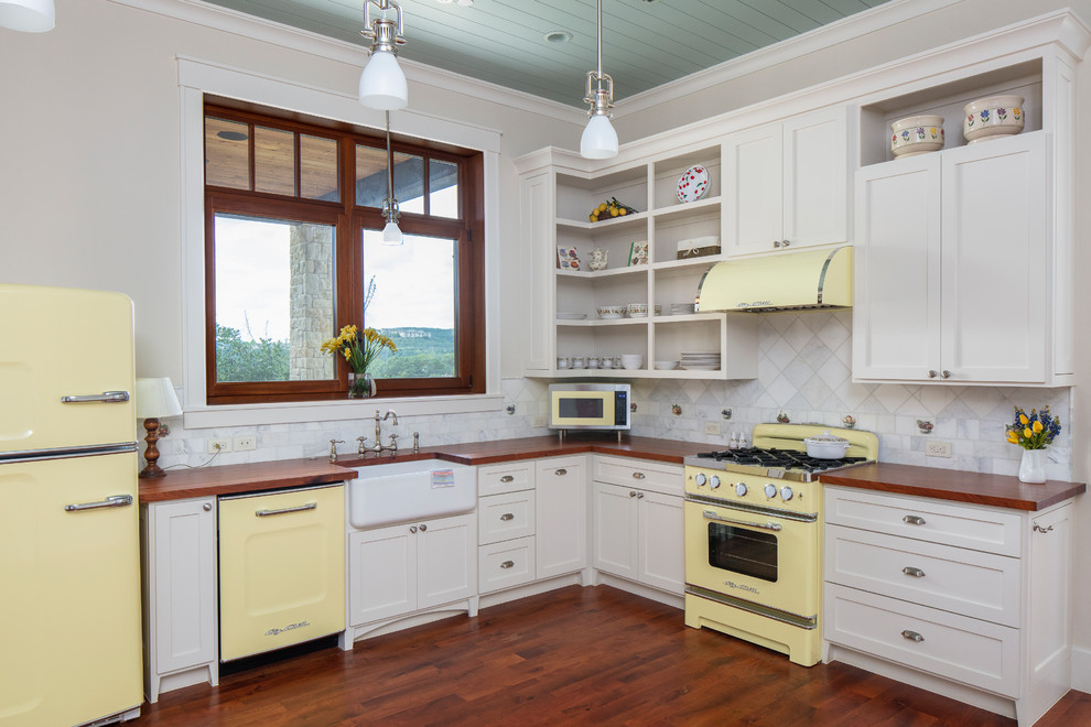 Traditional l-shaped kitchen in Austin with a farmhouse sink, shaker cabinets, white cabinets, wood benchtops, multi-coloured splashback, marble splashback, coloured appliances, medium hardwood floors, no island, brown floor and brown benchtop.