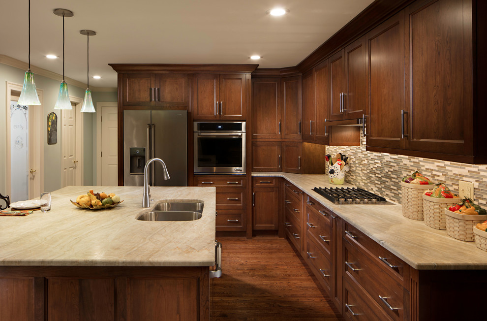 Inspiration for a mid-sized traditional l-shaped eat-in kitchen in Charlotte with a double-bowl sink, recessed-panel cabinets, brown cabinets, granite benchtops, beige splashback, glass tile splashback, stainless steel appliances, dark hardwood floors, with island, brown floor and beige benchtop.