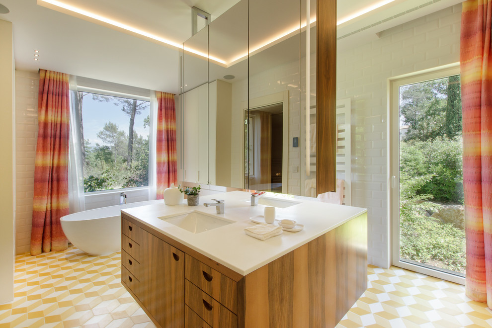 This is an example of a midcentury master bathroom in Nice with flat-panel cabinets, medium wood cabinets, a freestanding tub, white tile, subway tile, white walls, mosaic tile floors, an undermount sink, yellow floor and white benchtops.