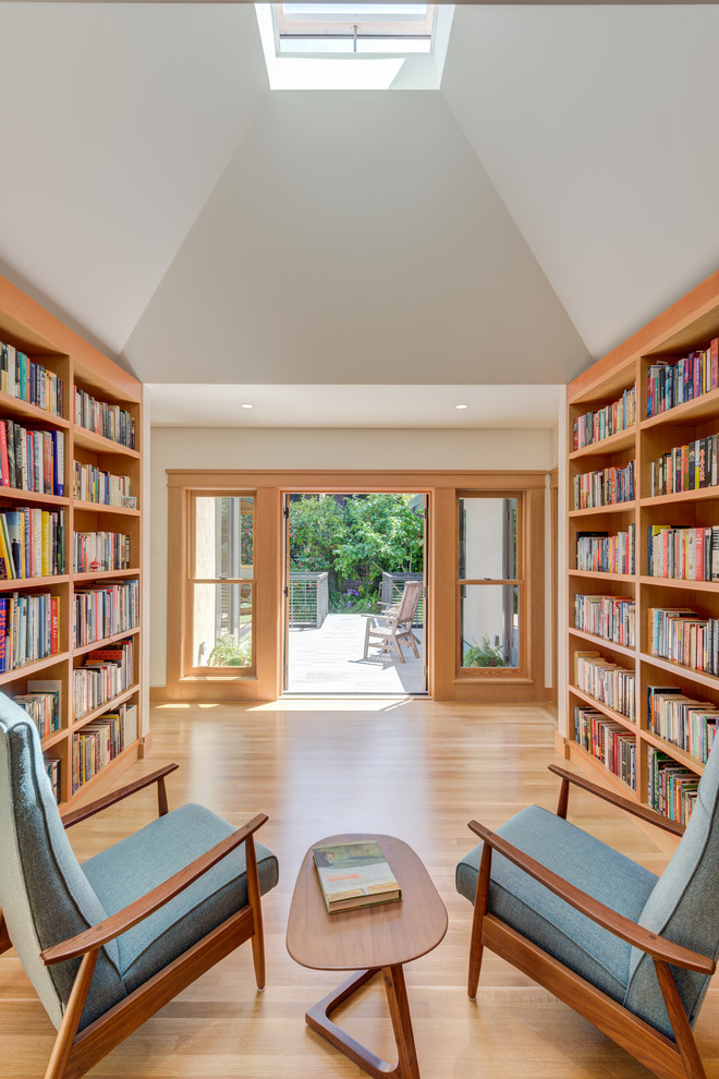This is an example of an arts and crafts family room in San Francisco with a library, white walls, light hardwood floors and beige floor.
