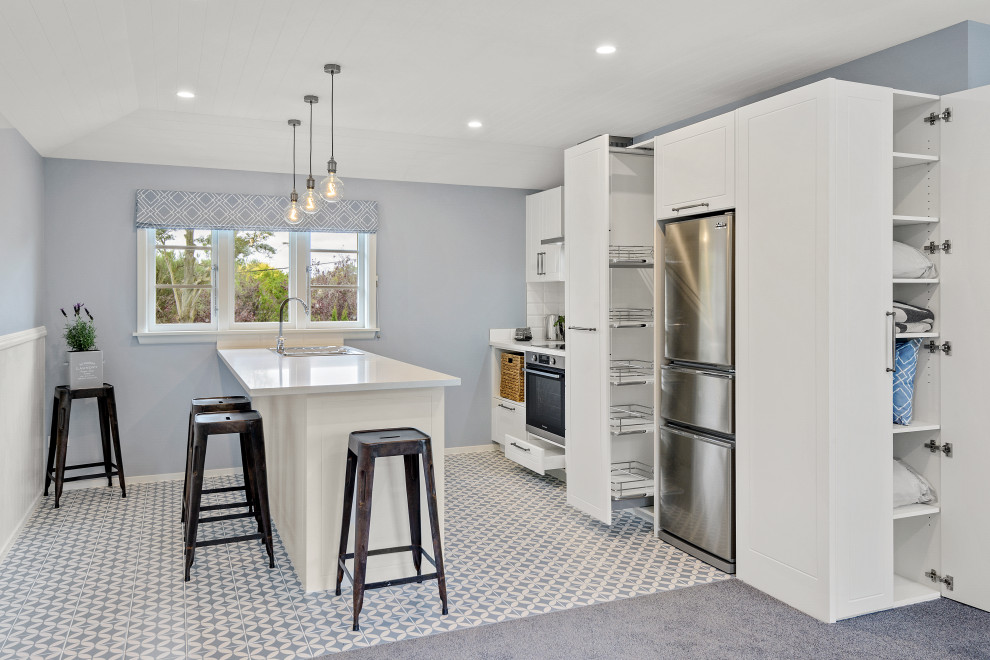 Inspiration for a small traditional galley kitchen/diner in Christchurch with a built-in sink, recessed-panel cabinets, white cabinets, engineered stone countertops, white splashback, porcelain splashback, stainless steel appliances, ceramic flooring, an island, multi-coloured floors, multicoloured worktops and a vaulted ceiling.