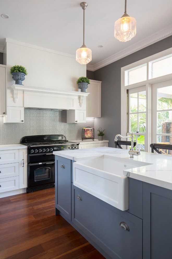 Design ideas for a mid-sized traditional l-shaped eat-in kitchen in Sydney with a farmhouse sink, shaker cabinets, white cabinets, quartz benchtops, grey splashback, metal splashback, black appliances, medium hardwood floors, with island, brown floor and multi-coloured benchtop.