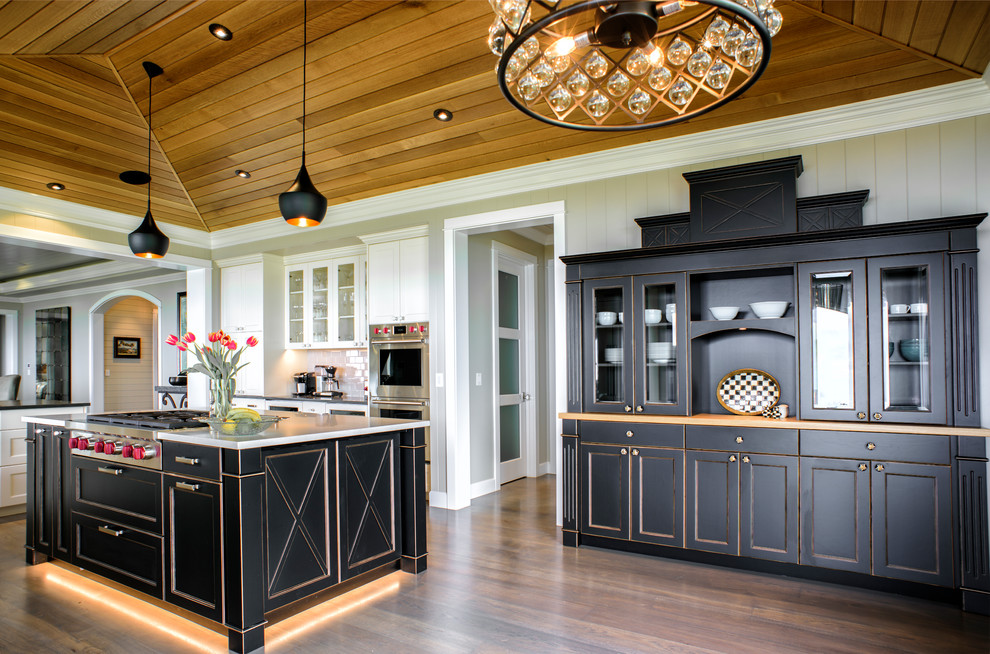 This is an example of a transitional kitchen in Other with recessed-panel cabinets, black cabinets, white splashback, stainless steel appliances, medium hardwood floors, with island and brown floor.