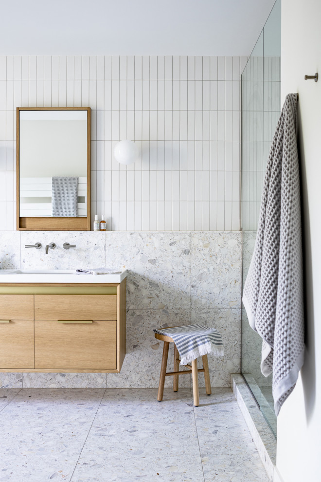 Cette photo montre une grande salle de bain principale et blanche et bois moderne en bois clair avec une douche, un carrelage blanc, des carreaux de céramique, un mur blanc, un sol en terrazzo, un lavabo encastré, un plan de toilette en quartz modifié, un sol gris, un plan de toilette blanc, meuble double vasque, meuble-lavabo suspendu et un placard à porte plane.