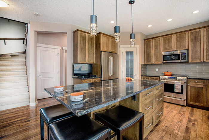 Mid-sized mountain style u-shaped medium tone wood floor and brown floor eat-in kitchen photo in Calgary with an undermount sink, shaker cabinets, medium tone wood cabinets, granite countertops, gray backsplash, glass tile backsplash, stainless steel appliances and an island