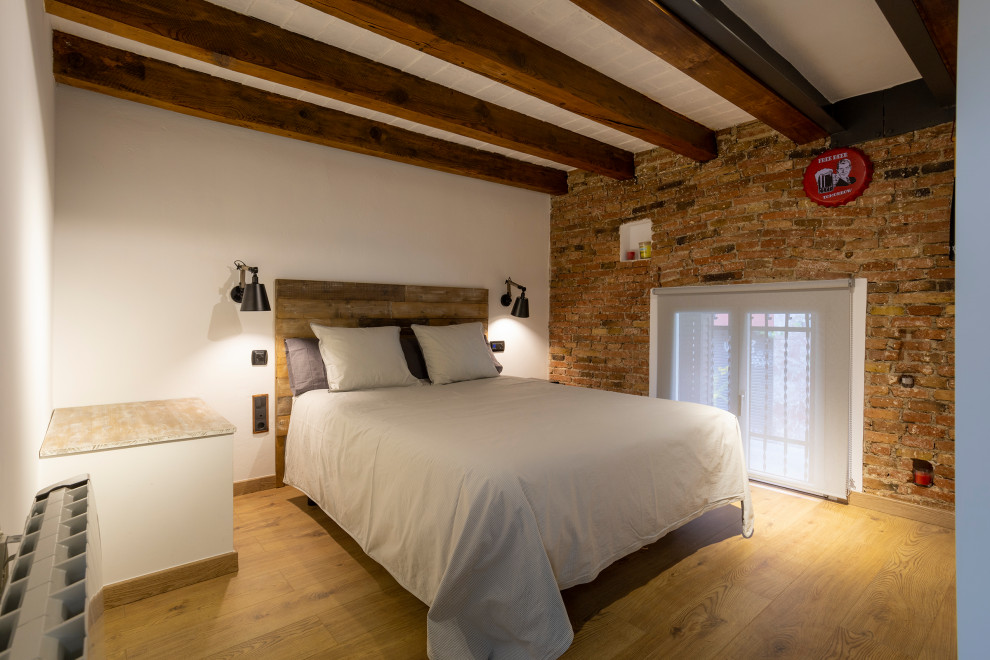 Photo of a medium sized urban guest bedroom in Barcelona with brown floors, exposed beams, white walls, medium hardwood flooring and brick walls.