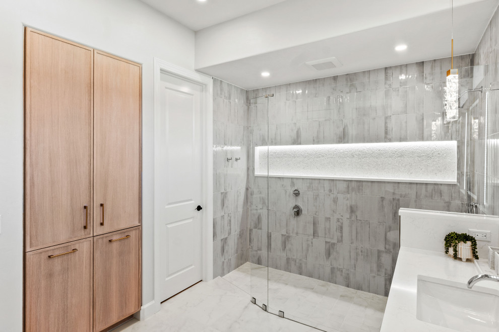 Walk-in shower - transitional master gray tile and porcelain tile porcelain tile, white floor and double-sink walk-in shower idea with shaker cabinets, light wood cabinets, a two-piece toilet, white walls, an undermount sink, quartz countertops, white countertops, a niche and a built-in vanity