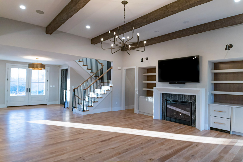 Design ideas for a large farmhouse open plan games room in St Louis with a home bar, white walls, light hardwood flooring, a standard fireplace, a tiled fireplace surround, a wall mounted tv, brown floors and exposed beams.