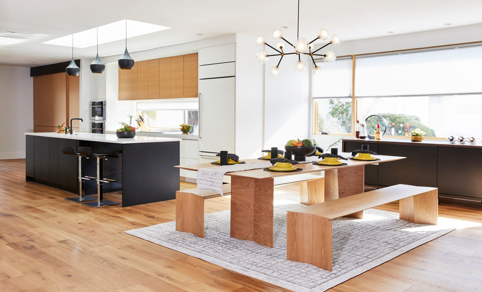 Design ideas for a large contemporary galley open plan kitchen in Philadelphia with an undermount sink, flat-panel cabinets, black cabinets, solid surface benchtops, window splashback, panelled appliances, light hardwood floors, with island and white benchtop.