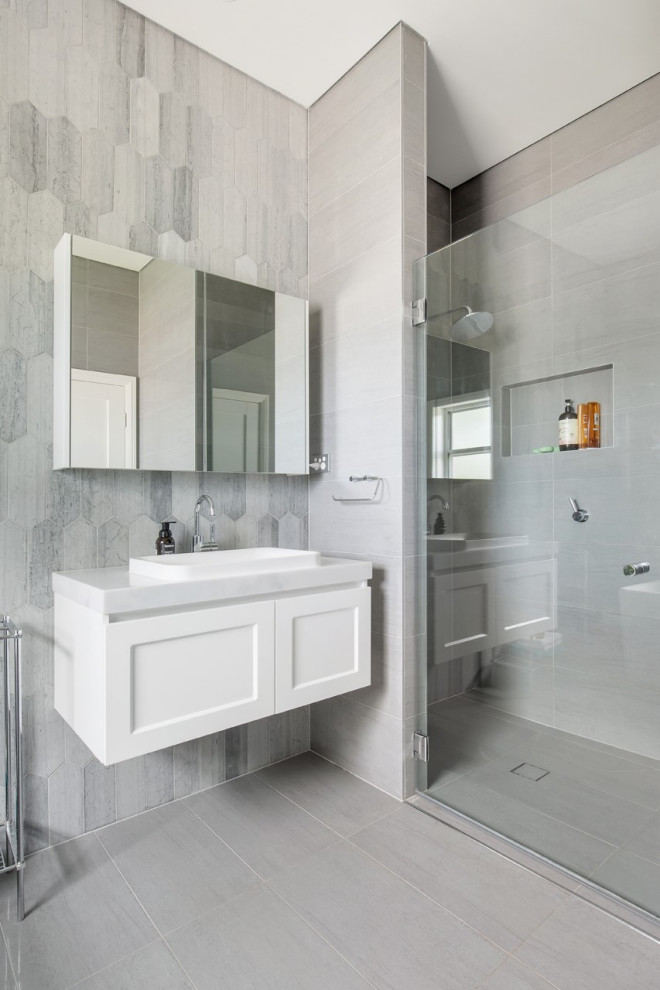 Inspiration for a mid-sized transitional 3/4 bathroom in Sydney with shaker cabinets, white cabinets, an alcove shower, a one-piece toilet, gray tile, limestone, grey walls, porcelain floors, a drop-in sink, marble benchtops, grey floor, a hinged shower door and grey benchtops.
