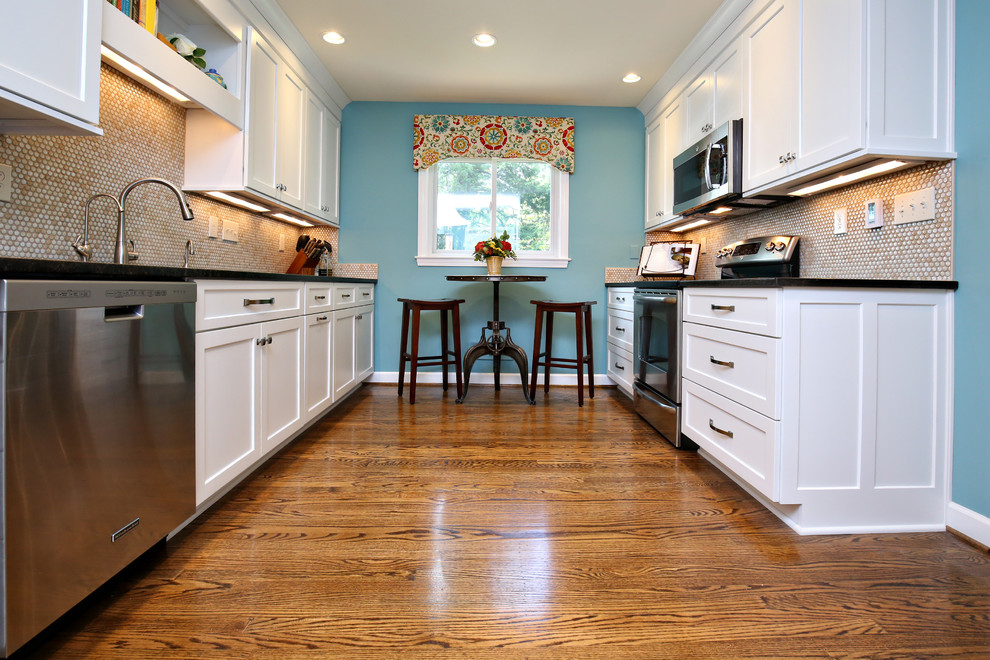 This is an example of a mid-sized traditional galley eat-in kitchen in Louisville with shaker cabinets, white cabinets, beige splashback, mosaic tile splashback, stainless steel appliances, medium hardwood floors, no island, brown floor, a double-bowl sink and granite benchtops.