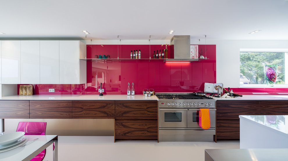This is an example of an expansive contemporary u-shaped kitchen in London with an undermount sink, flat-panel cabinets, solid surface benchtops, pink splashback, glass sheet splashback, stainless steel appliances and with island.