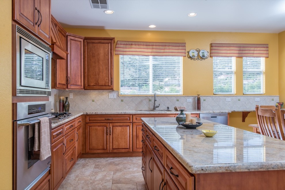 Traditional u-shaped eat-in kitchen in San Diego with a double-bowl sink, raised-panel cabinets, medium wood cabinets, granite benchtops, multi-coloured splashback and stainless steel appliances.