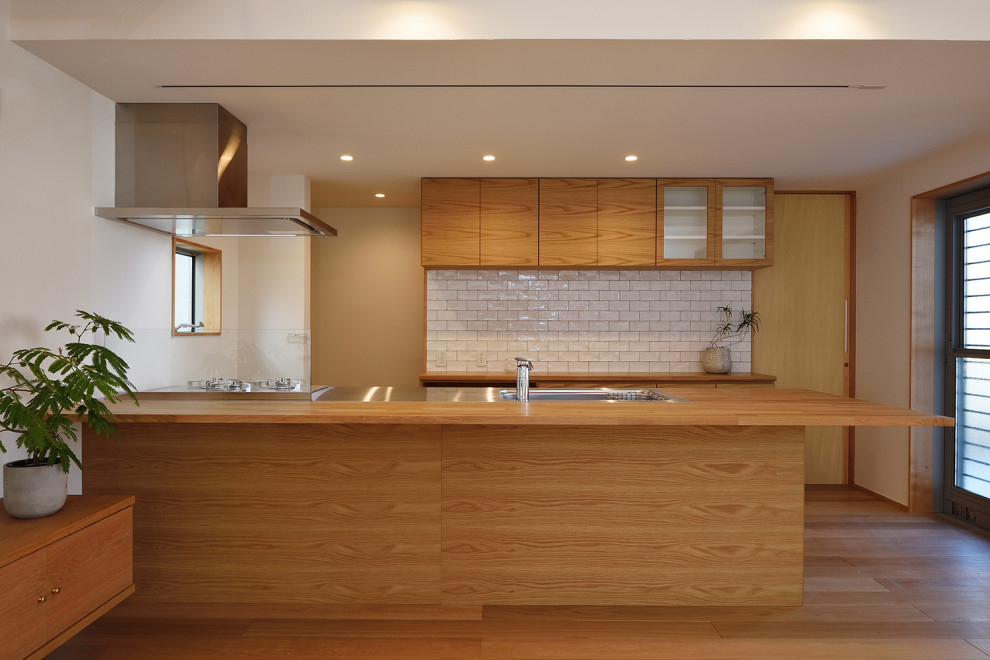 Inredning av ett nordiskt stort brun linjärt brunt kök med öppen planlösning, med en integrerad diskho, släta luckor, skåp i mellenmörkt trä, bänkskiva i rostfritt stål, vitt stänkskydd, rostfria vitvaror, mellanmörkt trägolv, en halv köksö och brunt golv