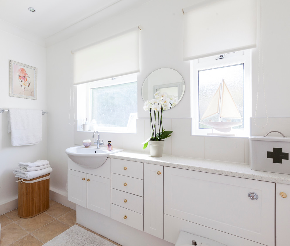Beach style bathroom in London with white cabinets, white tile, ceramic tile, white walls, linoleum floors, a drop-in sink, laminate benchtops and shaker cabinets.