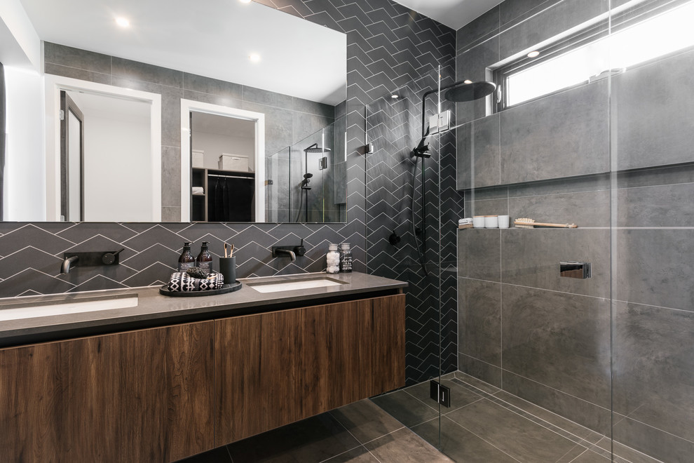 This is an example of a contemporary master bathroom in Adelaide with a hinged shower door, flat-panel cabinets, dark wood cabinets, a curbless shower, black tile, an undermount sink, grey floor and grey benchtops.