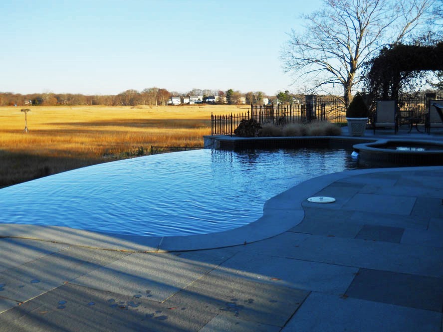 Photo of a large modern backyard custom-shaped infinity pool in New York with a hot tub and stamped concrete.