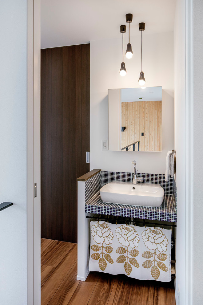 Inspiration for a modern powder room in Tokyo Suburbs with open cabinets, blue tile, white walls, medium hardwood floors, a vessel sink, tile benchtops and brown floor.