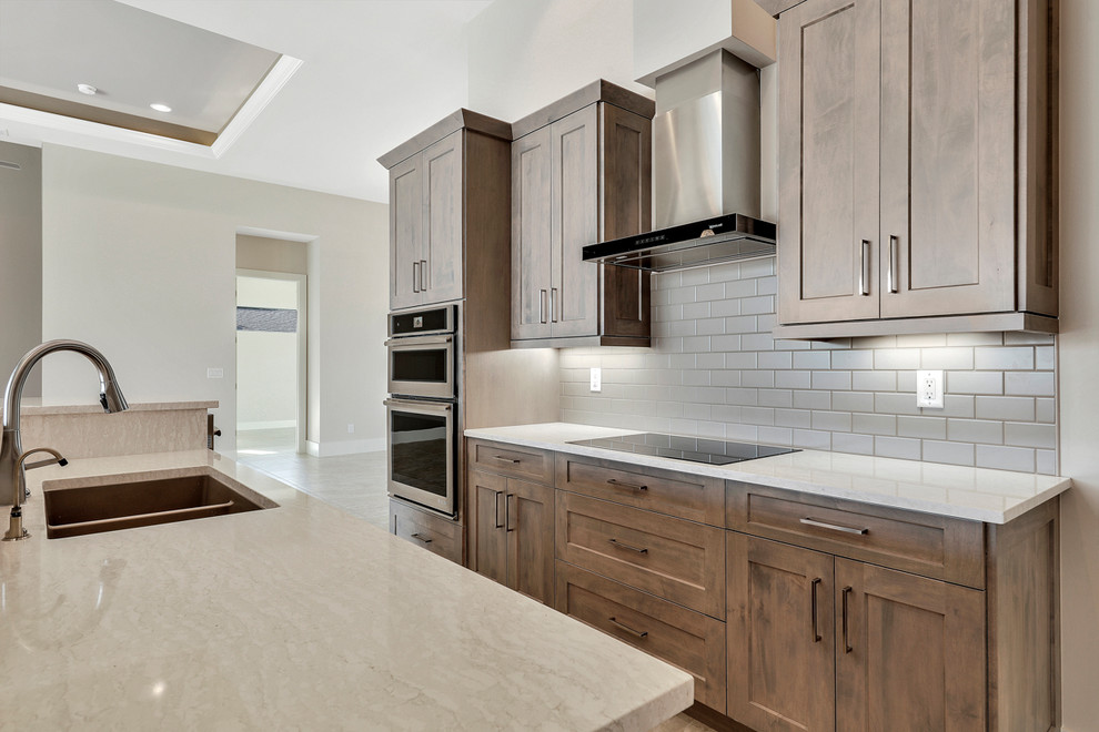 Example of a mid-sized transitional single-wall open concept kitchen design with a drop-in sink, recessed-panel cabinets, light wood cabinets, quartz countertops, gray backsplash, ceramic backsplash, stainless steel appliances, an island and beige countertops