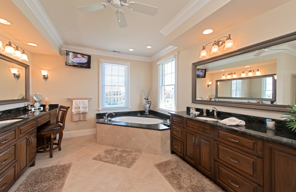This is an example of a mid-sized traditional master bathroom in Other with an undermount sink, raised-panel cabinets, granite benchtops, a corner tub, beige tile, porcelain tile, beige walls, porcelain floors, dark wood cabinets and beige floor.