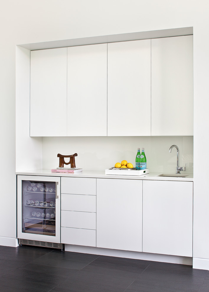 Mid-sized modern single-wall wet bar in New York with an undermount sink, flat-panel cabinets, white cabinets, solid surface benchtops, porcelain floors and black floor.