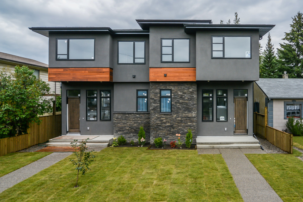 This is an example of a large contemporary two-storey stucco grey duplex exterior in Calgary with a flat roof and a metal roof.