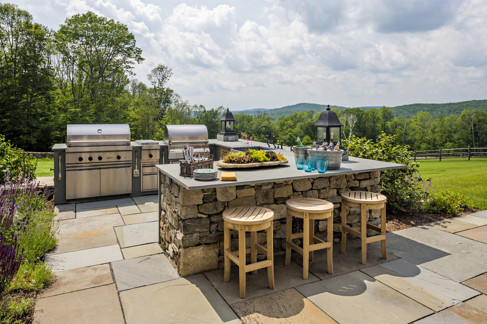 This is an example of an expansive traditional backyard patio in New York with an outdoor kitchen, natural stone pavers and no cover.