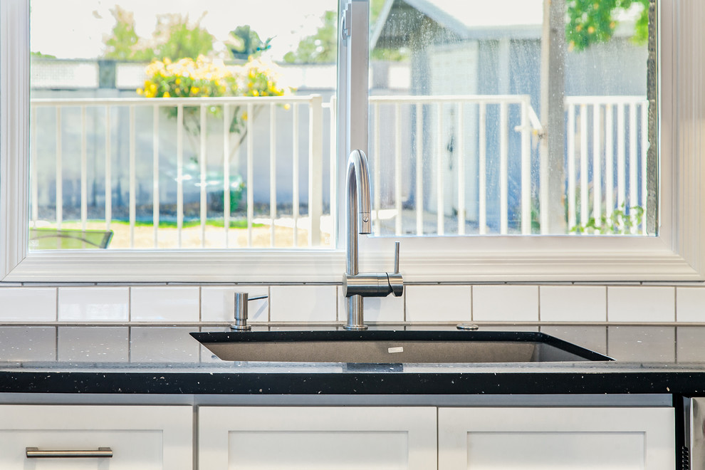 Example of a large transitional l-shaped porcelain tile and brown floor eat-in kitchen design in Phoenix with an undermount sink, recessed-panel cabinets, white cabinets, quartz countertops, black backsplash, ceramic backsplash, stainless steel appliances and an island