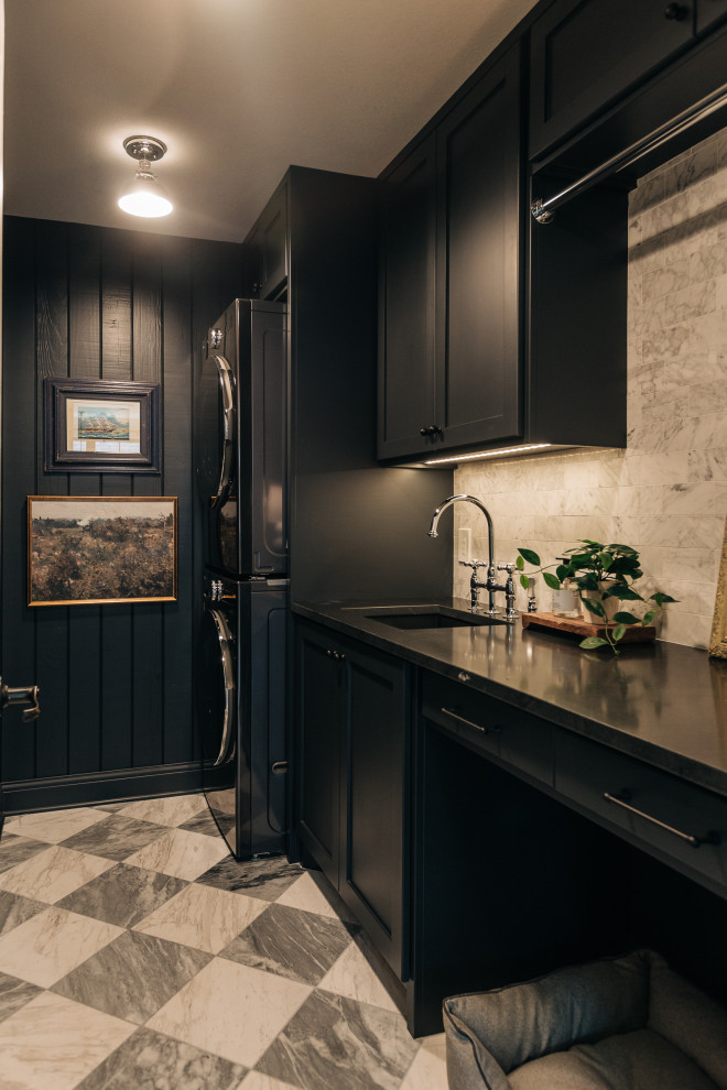 This is an example of a transitional laundry room in Dallas with an undermount sink, blue cabinets, quartzite benchtops, white splashback, marble splashback, blue walls, porcelain floors, a stacked washer and dryer, black benchtop and planked wall panelling.