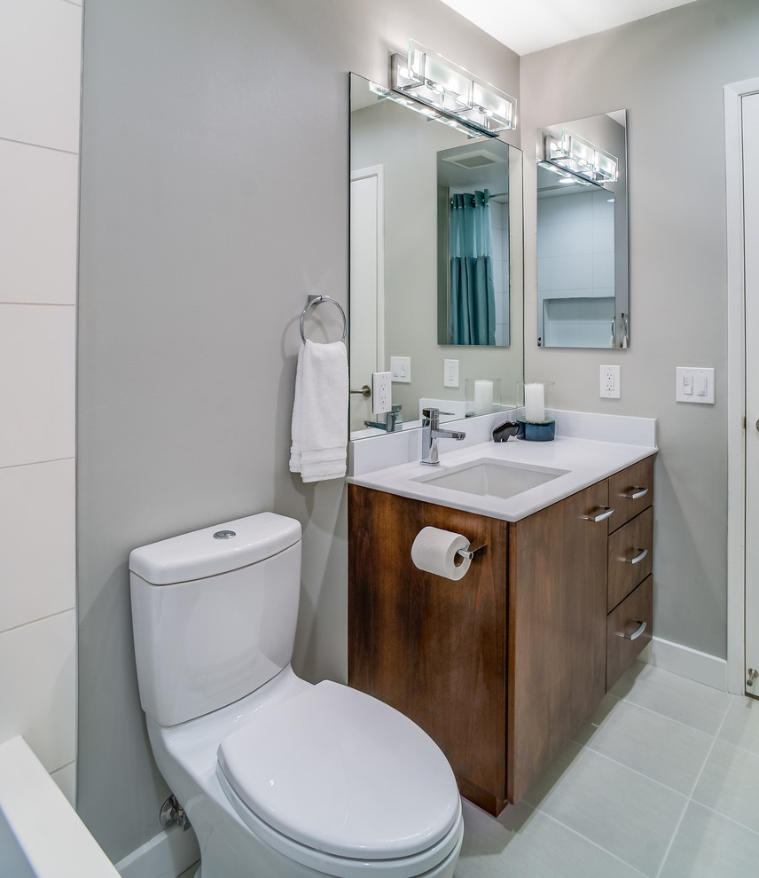 This is an example of a mid-sized modern bathroom in San Francisco with an undermount sink, flat-panel cabinets, dark wood cabinets, engineered quartz benchtops, an alcove tub, a shower/bathtub combo, a two-piece toilet, white tile, porcelain tile, grey walls and porcelain floors.