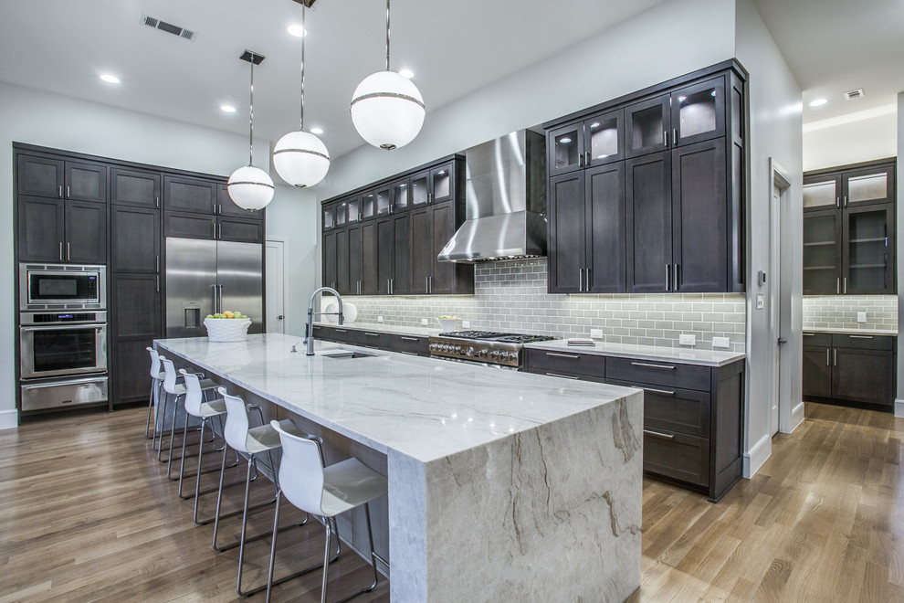 Design ideas for a transitional l-shaped kitchen in Dallas with an undermount sink, shaker cabinets, dark wood cabinets, grey splashback, subway tile splashback, stainless steel appliances, medium hardwood floors, with island and brown floor.