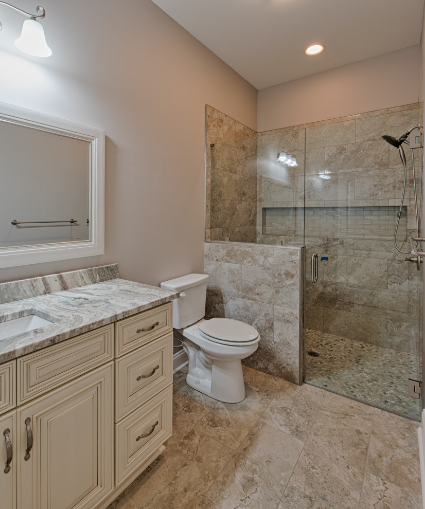 Photo of a large country bathroom in Atlanta with shaker cabinets, dark wood cabinets, an alcove shower, beige tile, limestone, beige walls, limestone floors, an undermount sink, granite benchtops, beige floor, a hinged shower door, multi-coloured benchtops and a built-in vanity.
