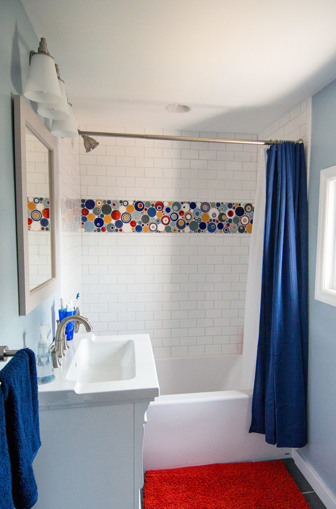 Photo of a small eclectic kids bathroom in Minneapolis with recessed-panel cabinets, white cabinets, a shower/bathtub combo, a one-piece toilet, multi-coloured tile, white tile, mosaic tile, blue walls, a drop-in tub, ceramic floors, an integrated sink and engineered quartz benchtops.