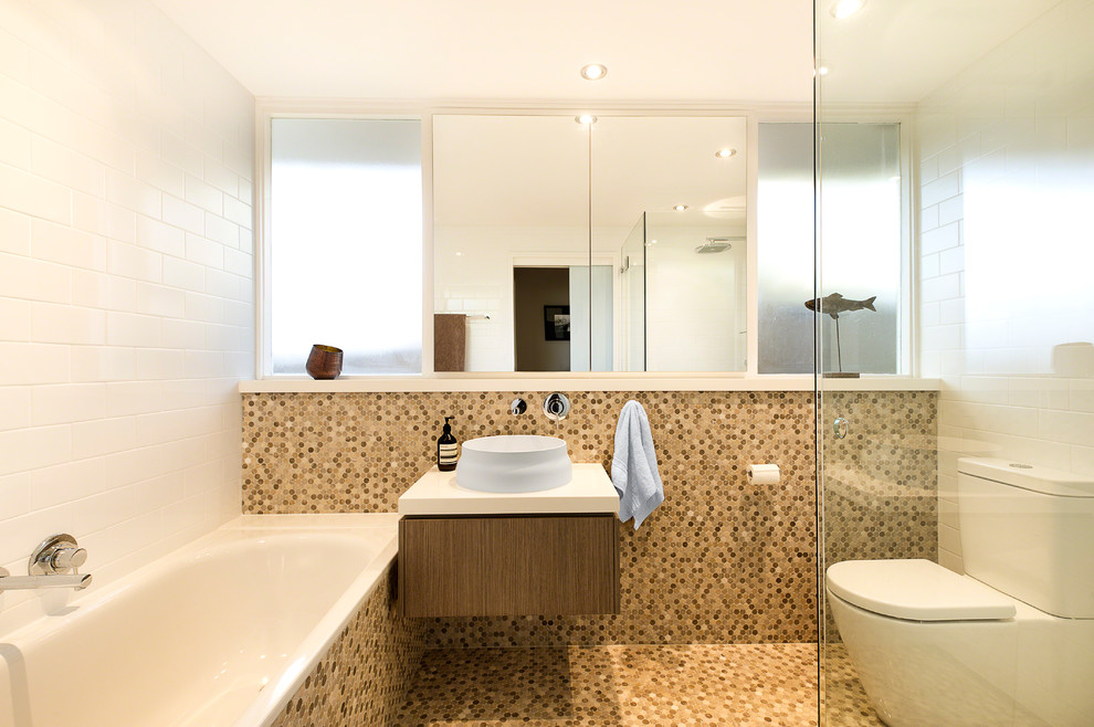 This is an example of a mid-sized contemporary 3/4 bathroom in Sydney with a vessel sink, flat-panel cabinets, medium wood cabinets, a drop-in tub, a corner shower, a two-piece toilet, white tile, subway tile, white walls and mosaic tile floors.