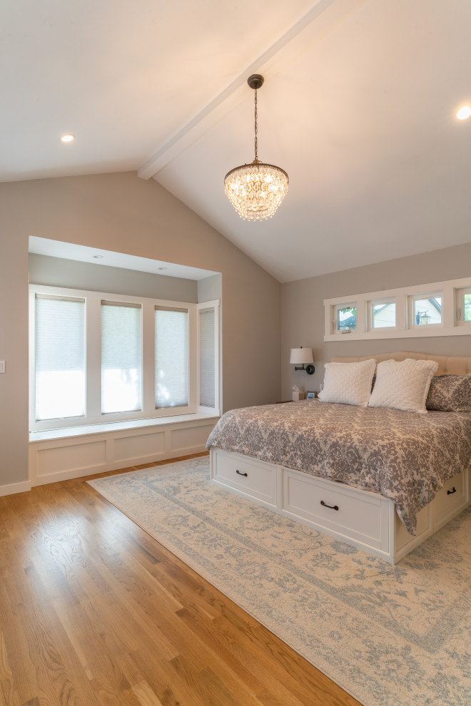 Modelo de dormitorio principal y abovedado de estilo americano de tamaño medio con paredes beige, suelo de madera clara y suelo rojo