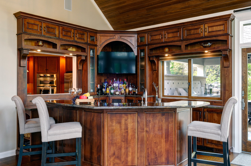 Mid-sized traditional u-shaped seated home bar in Columbus with an undermount sink, raised-panel cabinets, dark wood cabinets, granite benchtops and cork floors.