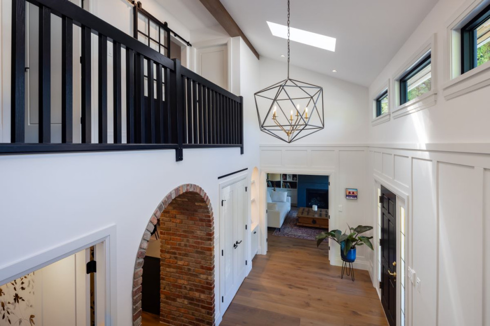 Example of a mid-sized transitional medium tone wood floor, brown floor and wall paneling foyer design in Vancouver with white walls and a black front door