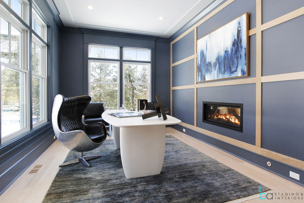 Photo of a large contemporary home office in New York with blue walls, light hardwood floors, a hanging fireplace, a freestanding desk, beige floor and panelled walls.
