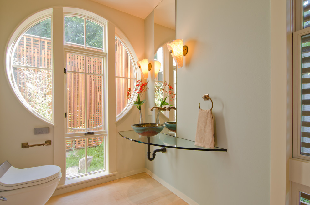 This is an example of a mid-sized contemporary powder room in Portland with a vessel sink, blue walls, light hardwood floors, glass benchtops and beige floor.