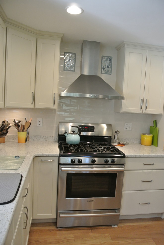 Inspiration for a transitional l-shaped medium tone wood floor eat-in kitchen remodel in Boston with an undermount sink, shaker cabinets, white cabinets, recycled glass countertops, white backsplash, subway tile backsplash, stainless steel appliances, a peninsula and white countertops