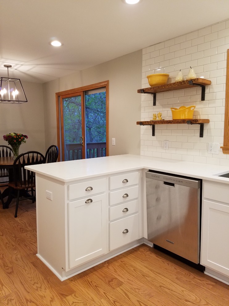 Example of a mid-sized transitional u-shaped medium tone wood floor and brown floor eat-in kitchen design with an undermount sink, shaker cabinets, white cabinets, quartz countertops, white backsplash, subway tile backsplash, stainless steel appliances and a peninsula