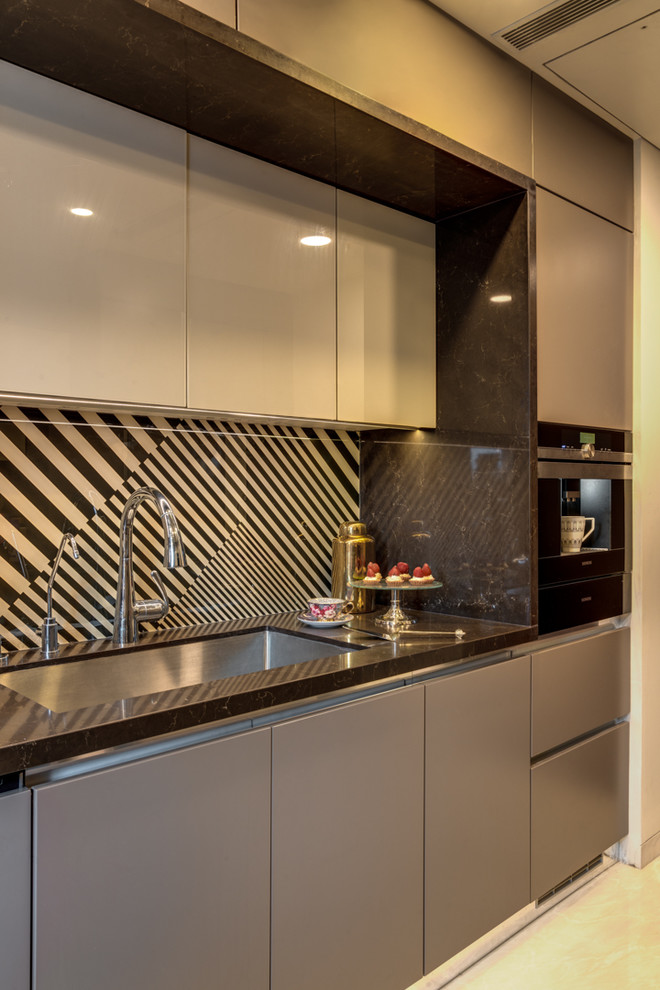 This is an example of a mid-sized contemporary galley separate kitchen in Mumbai with a drop-in sink, beige cabinets, quartz benchtops, beige splashback, glass tile splashback, panelled appliances, marble floors, no island, white floor and brown benchtop.